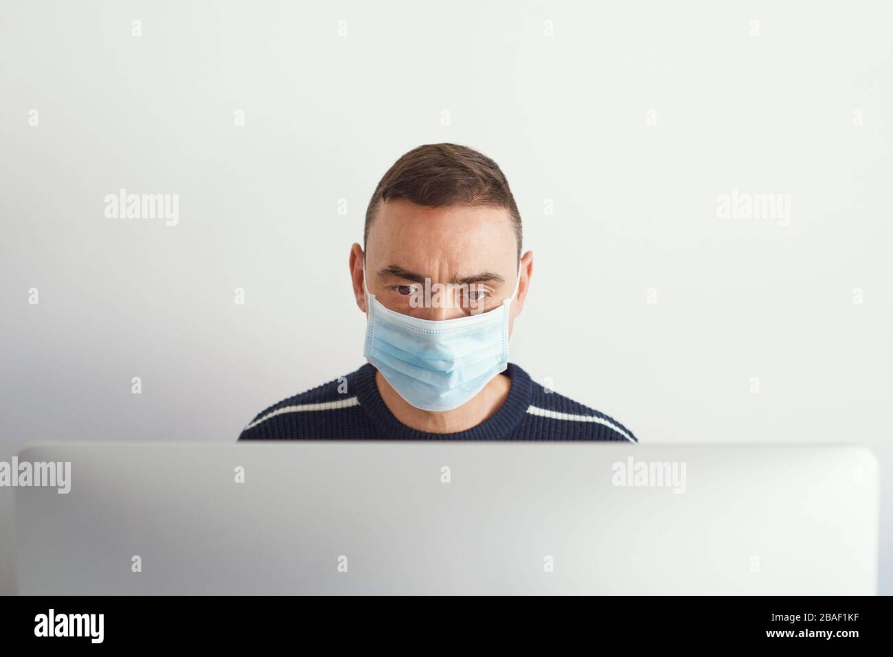 primo piano di un giovane caucasico al chiuso, con maschera chirurgica, con un computer Foto Stock