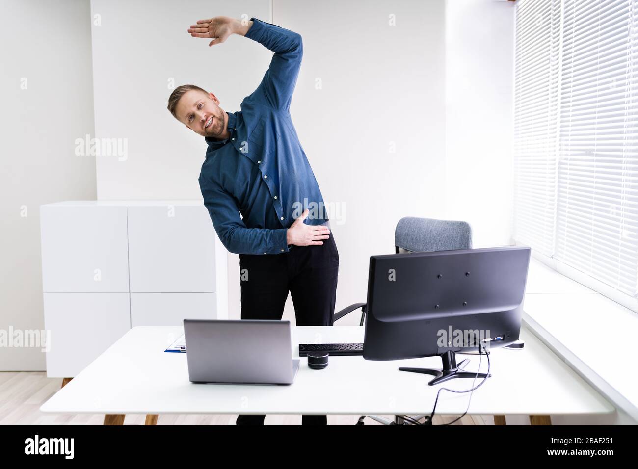 Giovane Imprenditore facendo esercizio di stretching in ufficio Foto Stock