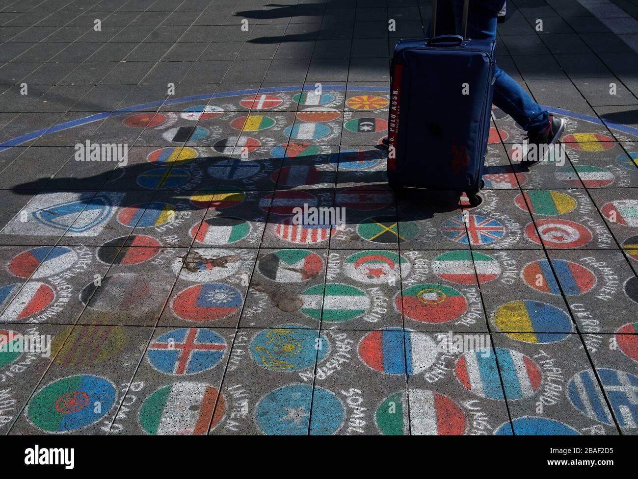 Bochum, Germania. 27 marzo 2020. Un uomo spinge la sua valigia sopra le bandiere di vari paesi, che sono stati dipinti con gesso sul pavimento della zona pedonale. A causa del virus della corona, il viaggio è attualmente possibile solo in misura molto limitata. Credit: Bernd Thissen/dpa/Alamy Live News Foto Stock
