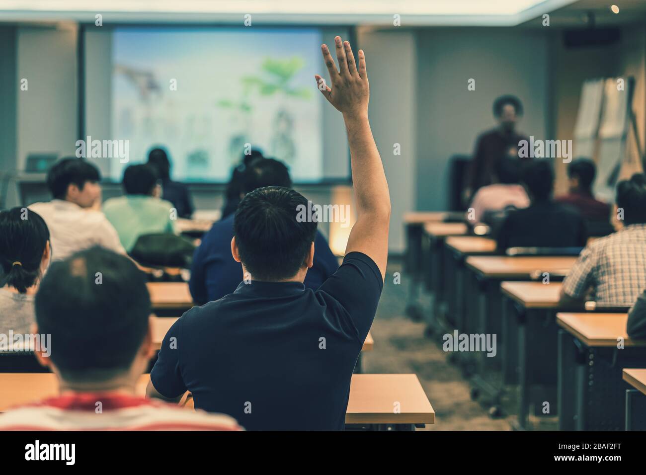 Vista posteriore del pubblico in risposta mano per rispondere alla domanda nella sala riunioni o nella sala conferenze sopra l'altoparlante asiatico sul palco, seminario Foto Stock