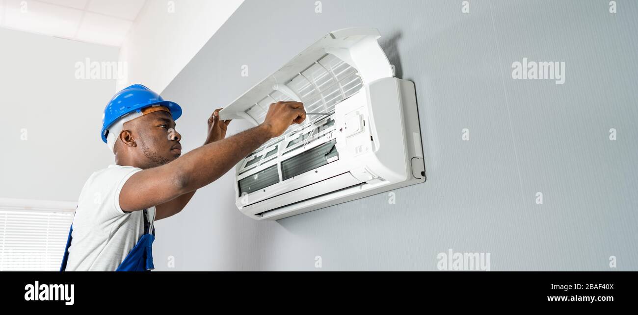 Felice giovane africano tecnico maschio riparare il condizionatore d'aria Foto Stock