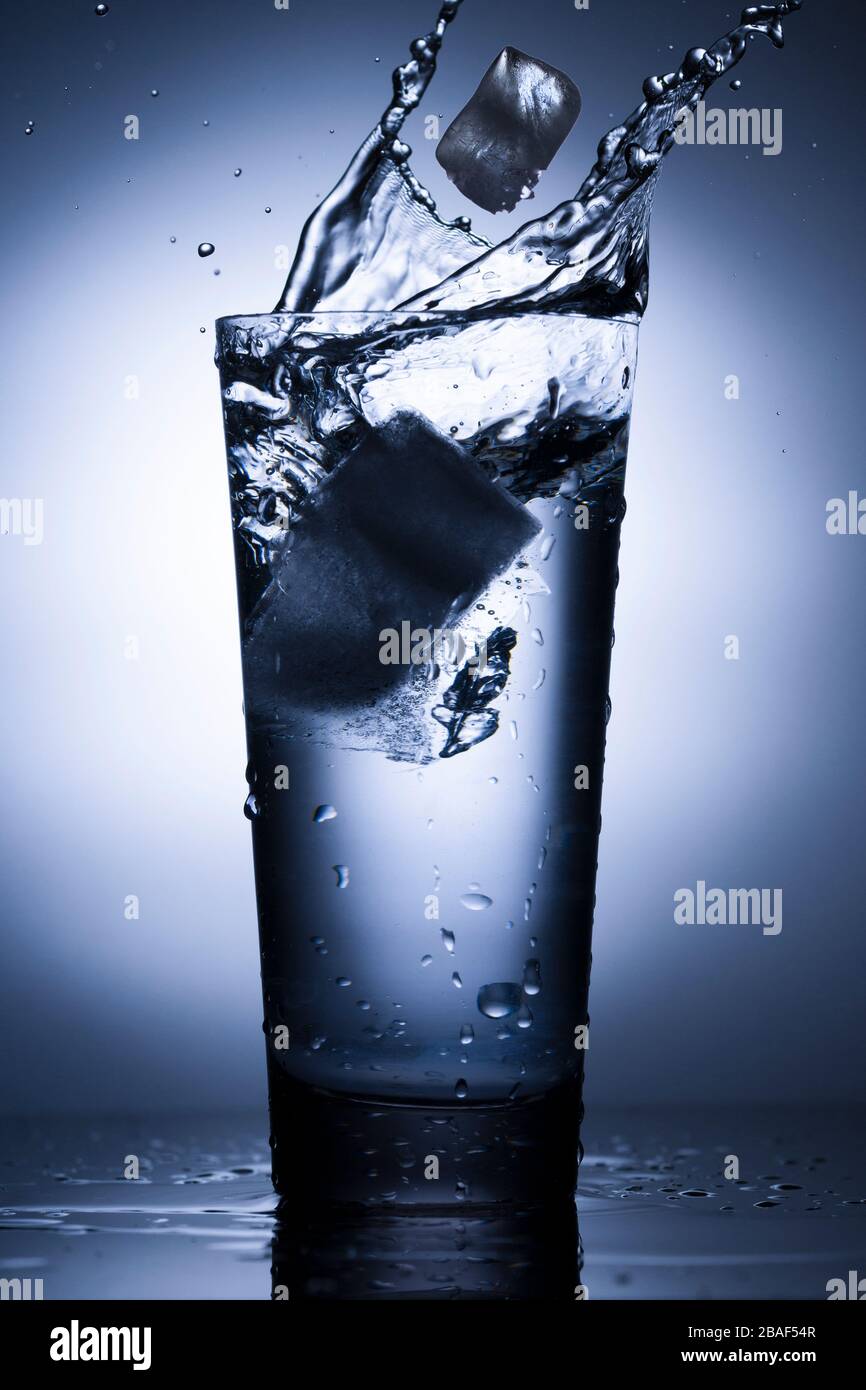 Bicchiere d'acqua con spruzzi e ghiaccio su sfondo blu. Foto Stock