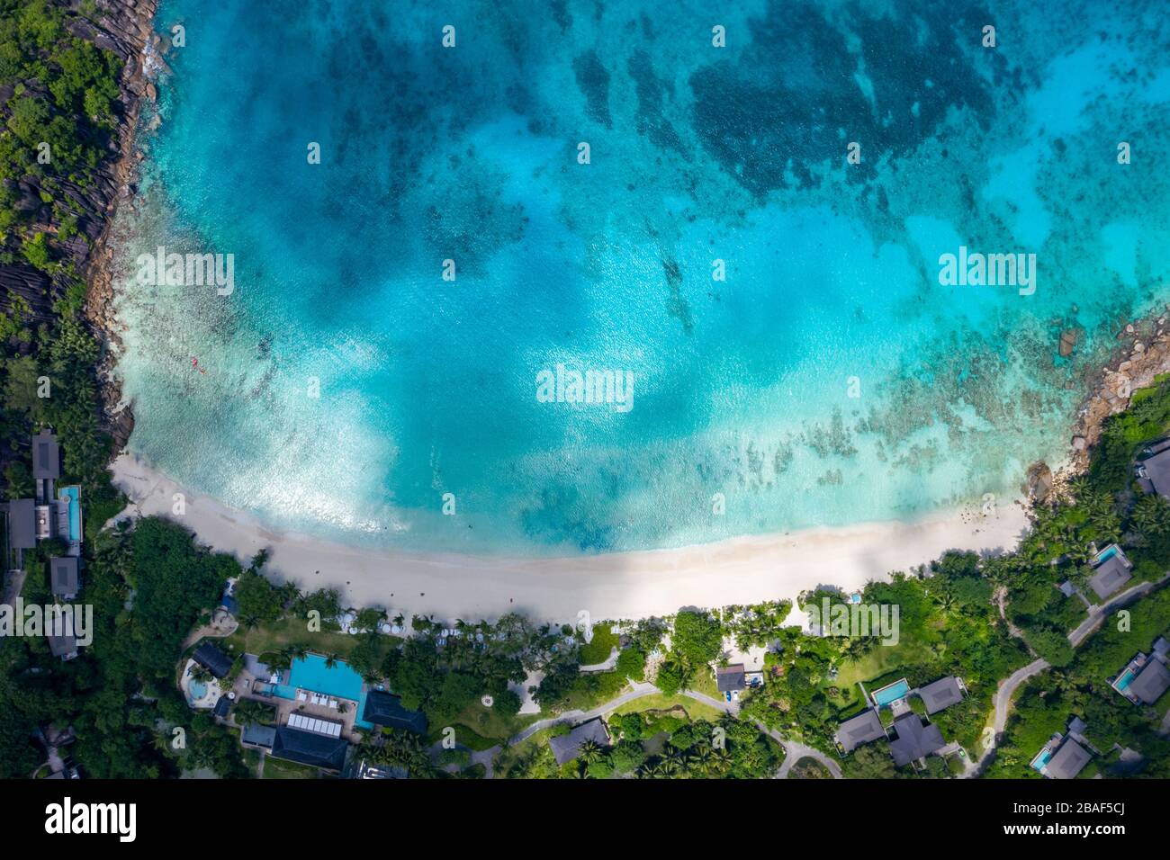 Vista aerea del resort sulla spiaggia tropicale con baia turchese e lussureggiante collina, Anse Petite, Mahe Island, Seychelles Foto Stock