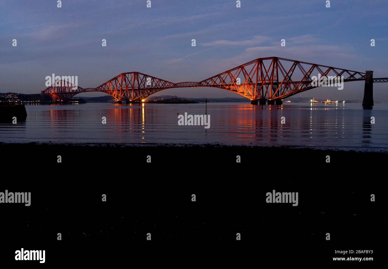 Illuminato il ponte ferroviario di fronte al Firth visto da South Queensferry di notte in inverno, Scozia, Regno Unito, Europa Foto Stock