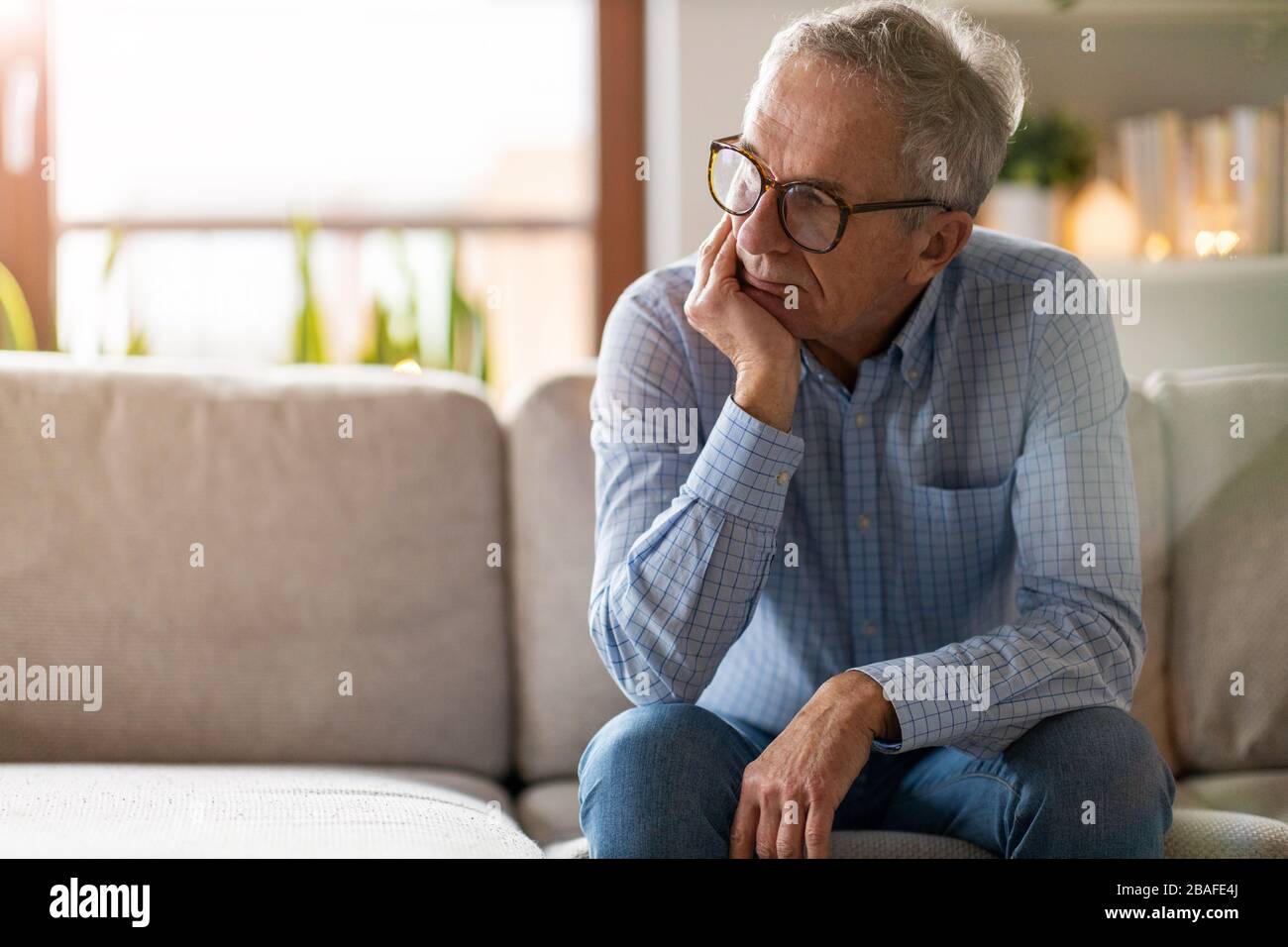 Preoccupato uomo anziano seduto da solo nella sua casa Foto Stock