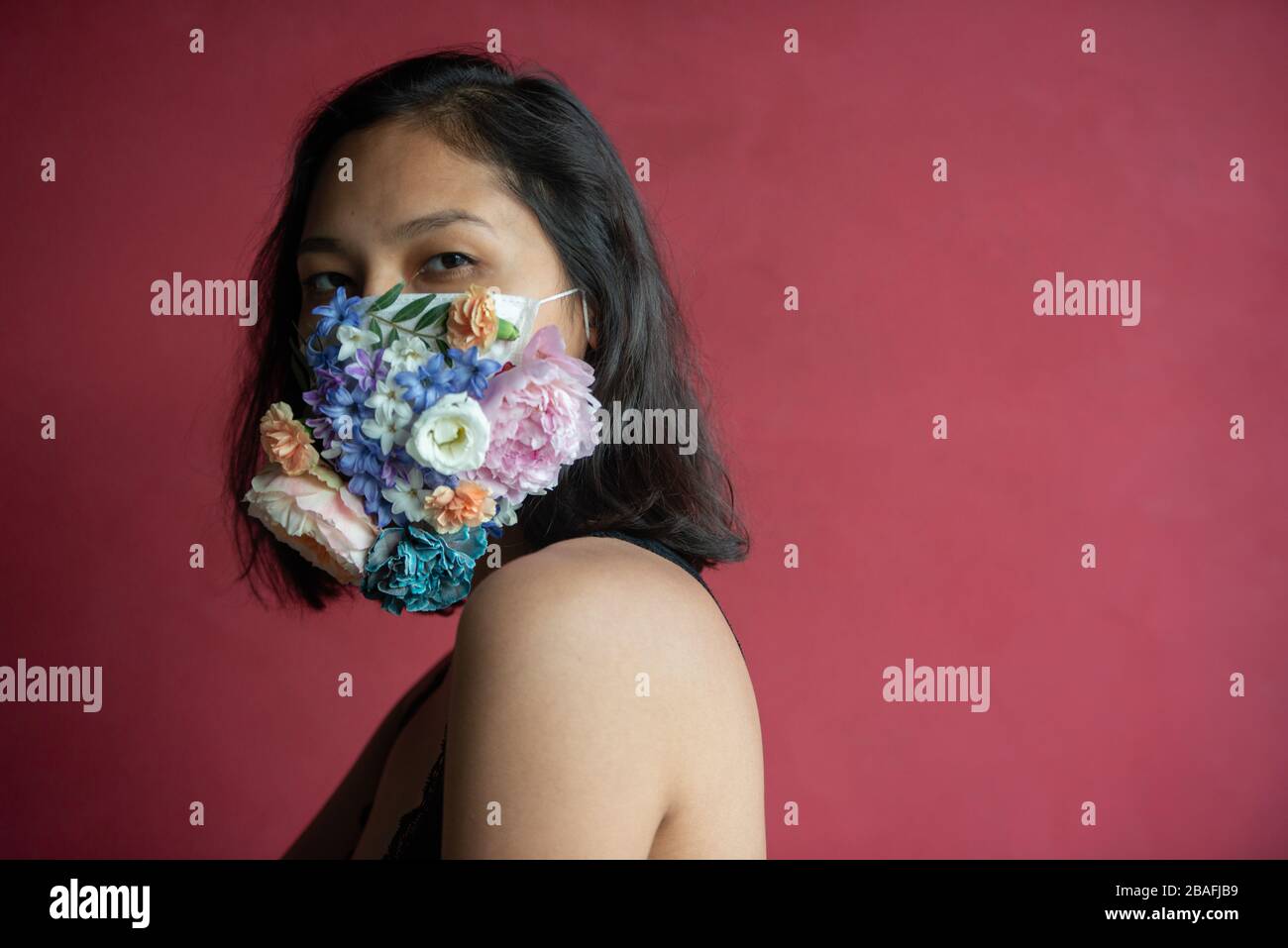Donna in maschera medica protettiva con fiori su sfondo rosso. Foto Stock