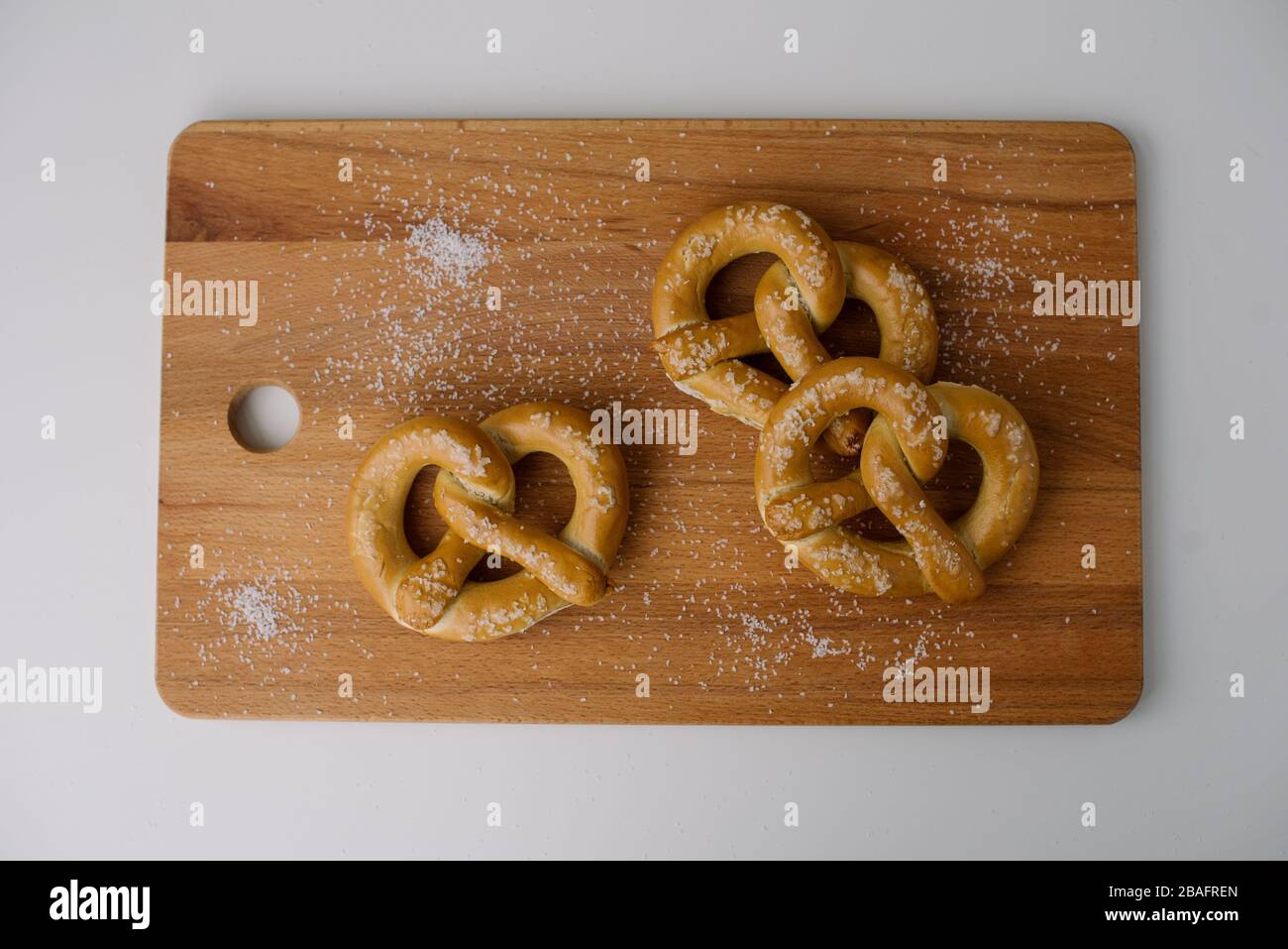 Tre pretzel morbidi su un tagliere di legno cosparso di sale su uno sfondo bianco. Foto Stock