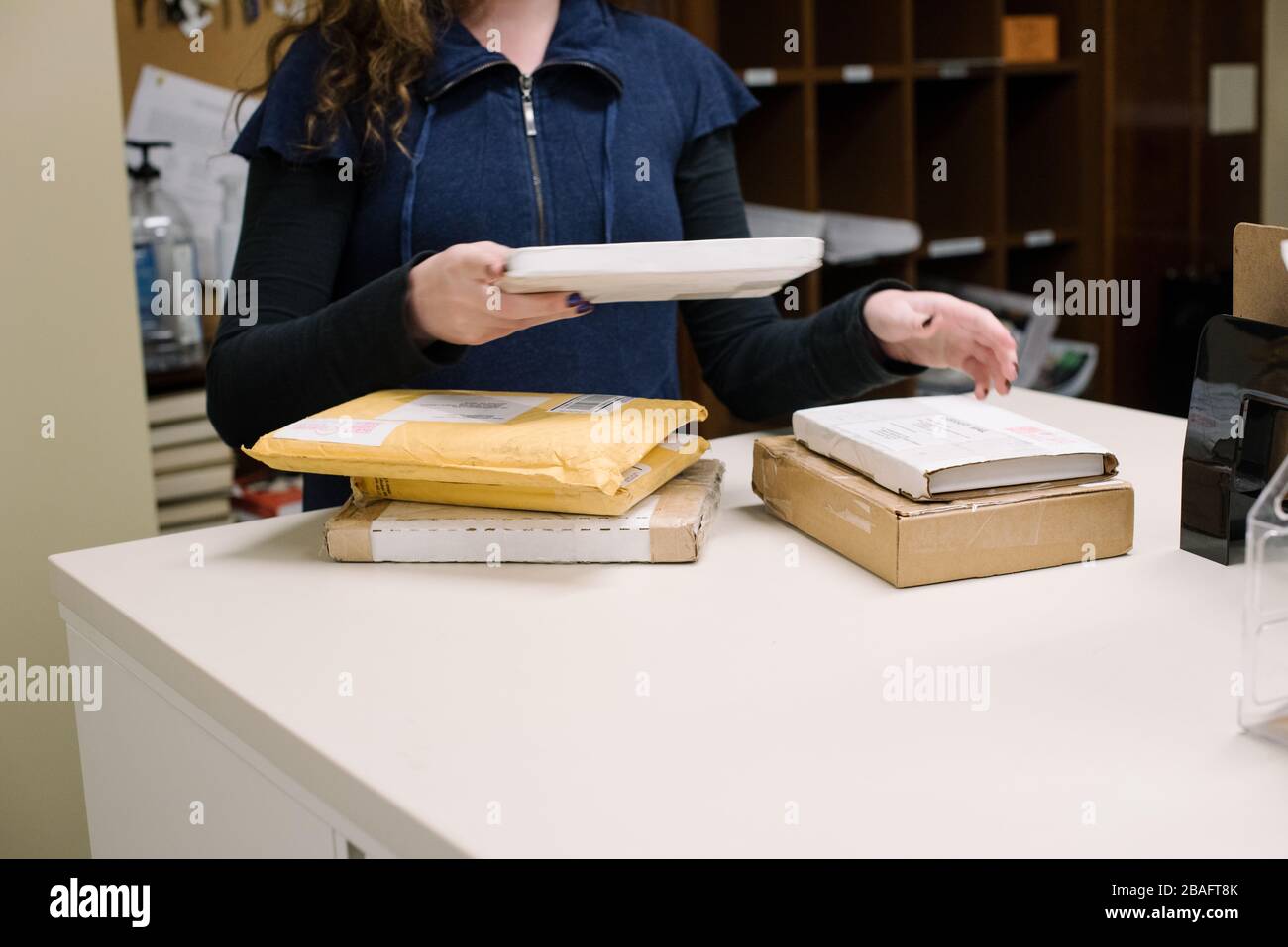 Donna mentre bibliotecaria (solo a mani) presso un banco di lavoro che impacchette i supporti in contenitori da consegnare ai clienti. Foto Stock