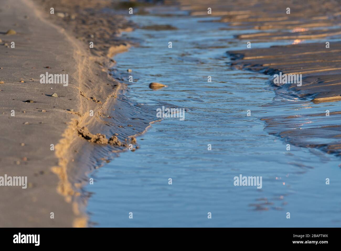 L'acqua dell'oceano scorre come un ruscello attraverso il canale scolpito naturalmente nella sabbia della spiaggia. Foto Stock