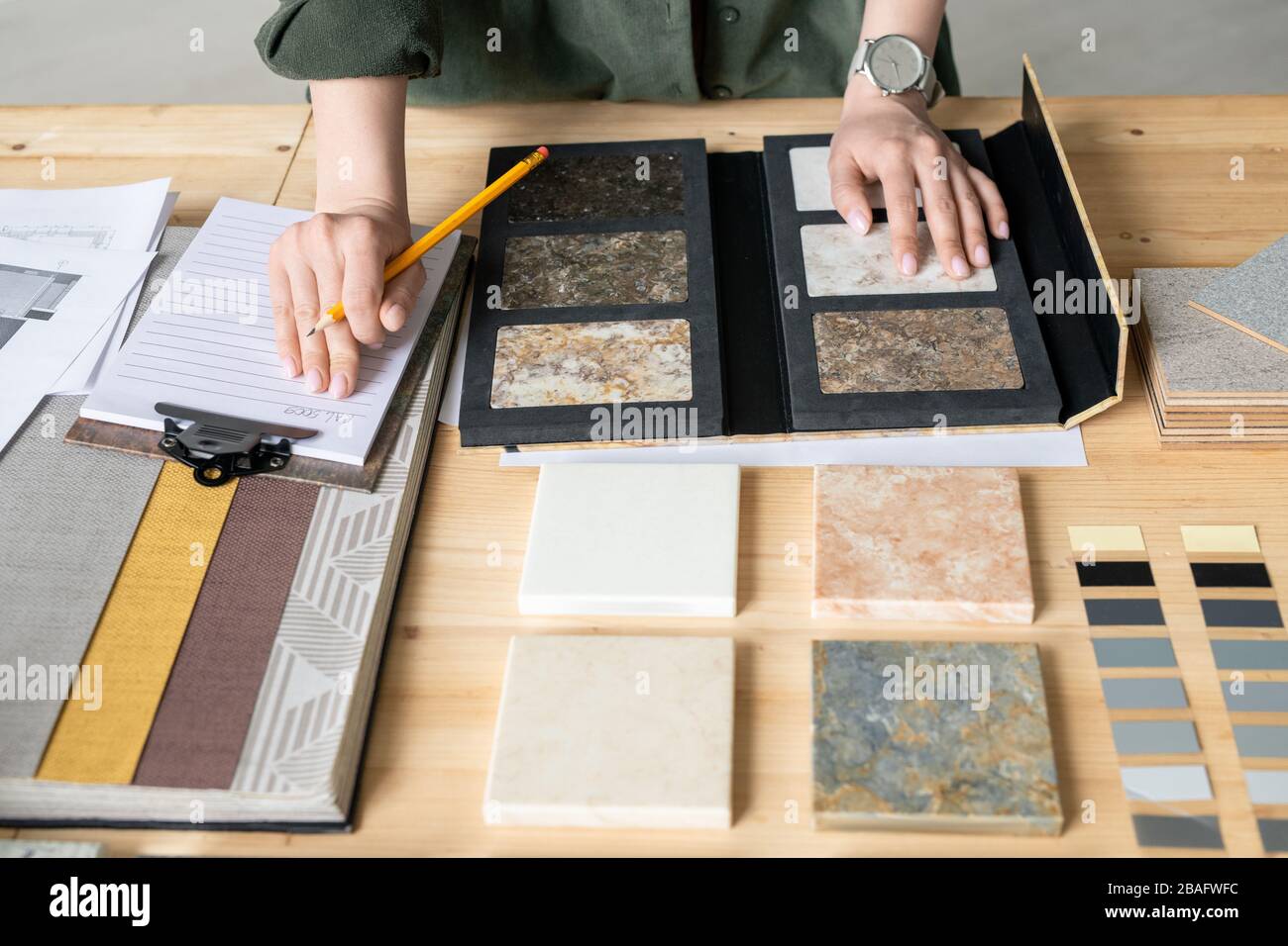 Mani di giovane donna che prende appunti su carta mentre sceglie campione di pannello dalla raccolta durante il lavoro su nuovo ordine Foto Stock