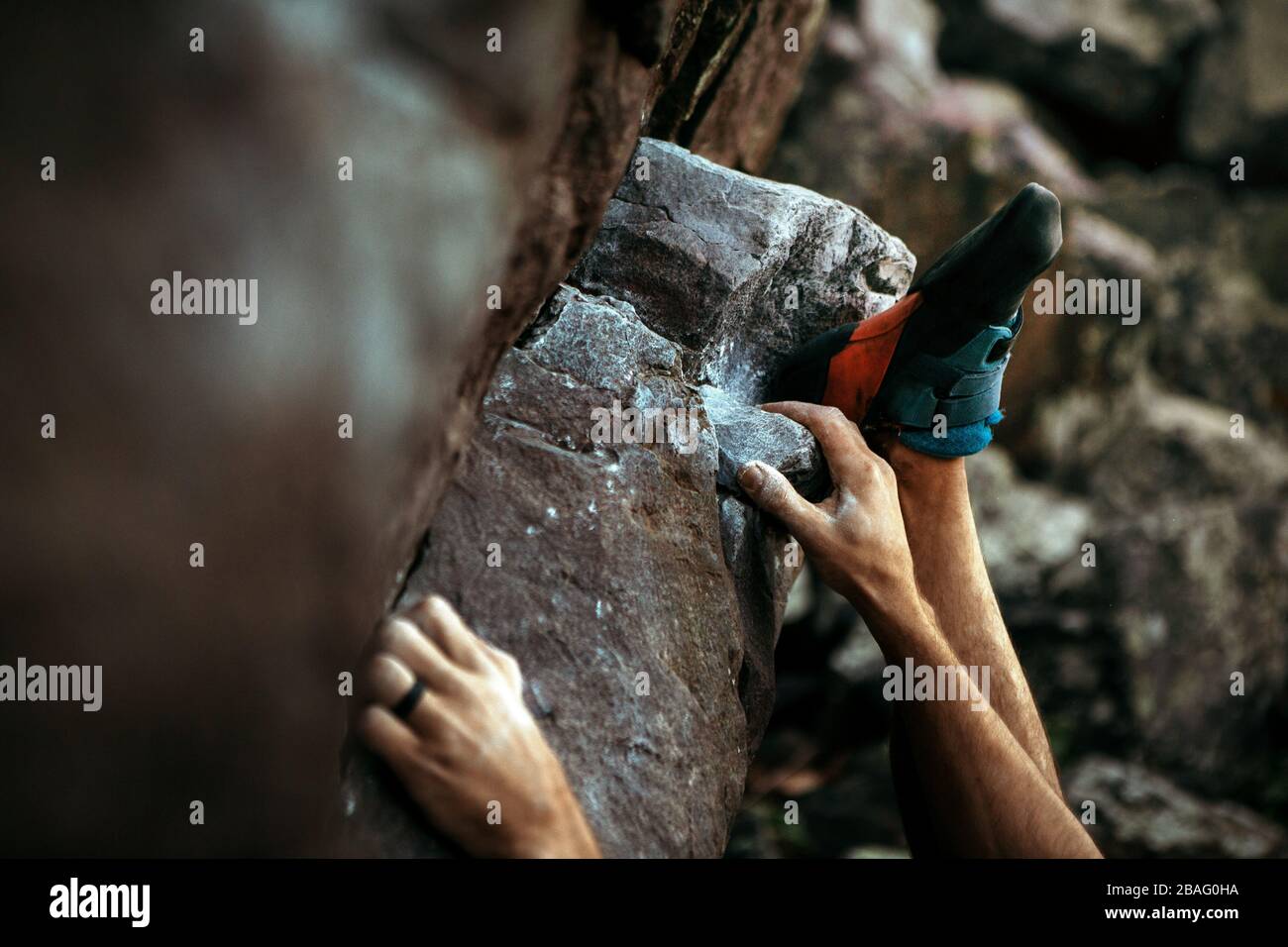 Primo piano di una mano di scalatore con una fascia nera per matrimoni e scarpe da arrampicata mentre si accende per salire su un masso di roccia Foto Stock