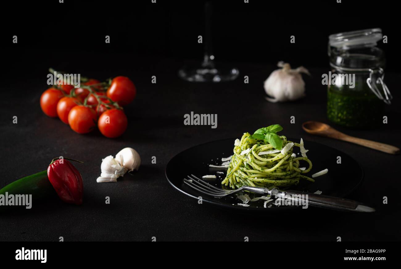 Spaghetti al pesto con salsa genovese verde con pomodori freschi su piatto nero e fondo nero con luce laterale Foto Stock