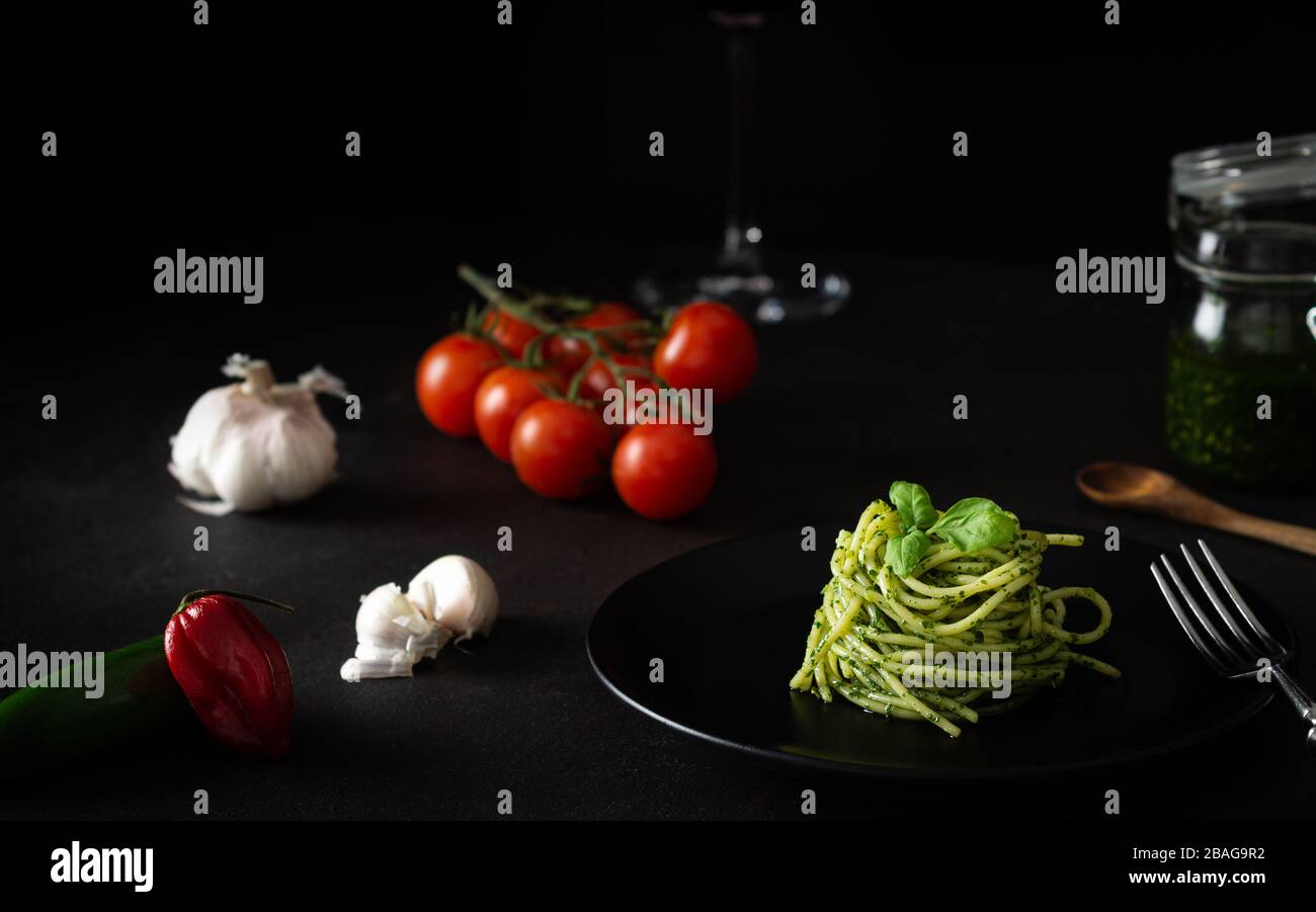 Spaghetti al pesto con salsa genovese verde con pomodori freschi su piatto nero e fondo nero con luce laterale Foto Stock