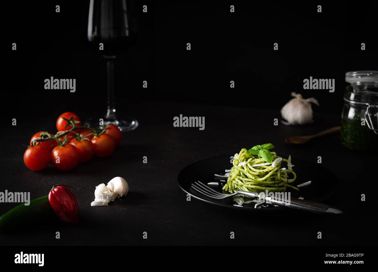 Spaghetti al pesto con salsa genovese verde con pomodori freschi su piatto nero e fondo nero con luce laterale Foto Stock