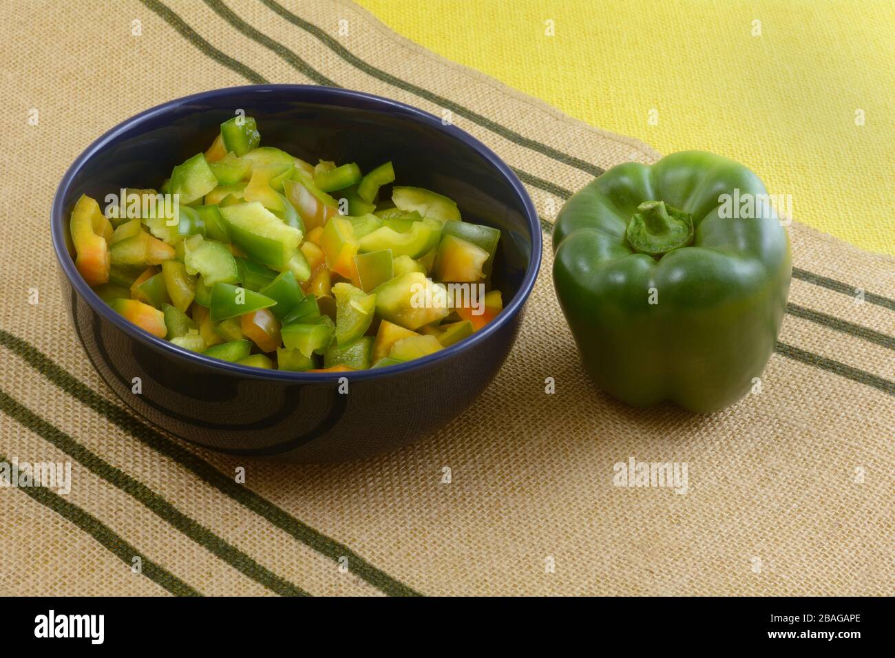Peperoni freschi tritati crudi in ciotola blu e peperone intero su stuoia marrone del posto Foto Stock