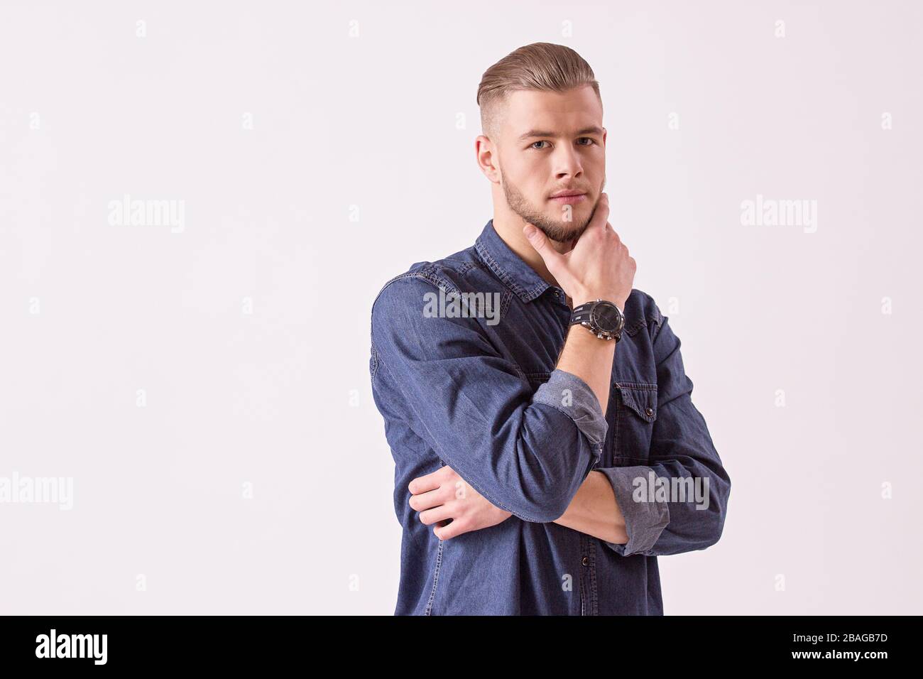 Ritratto di giovane uomo pensieroso che tiene la mano sul mento e che guarda alla macchina fotografica mentre isolato su sfondo bianco. Elegante, elegante e con bearded hippster Foto Stock