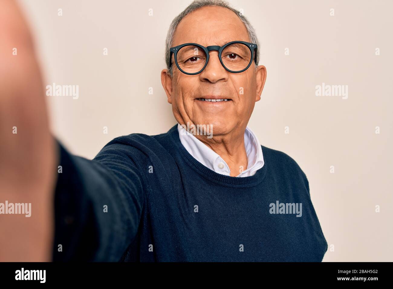Uomo anziano con i capelli grigi e gli occhiali che fanno il selfie con la macchina fotografica con un volto felice in piedi e sorridente con uno spettacolo di sorriso sicuro Foto Stock