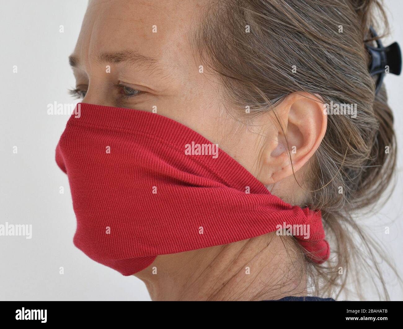 La donna caucasica si pone per la telecamera con la sua maschera facciale fai da te (realizzata da una vecchia maglietta) durante la pandemia del virus corona 2019-20 . Foto Stock