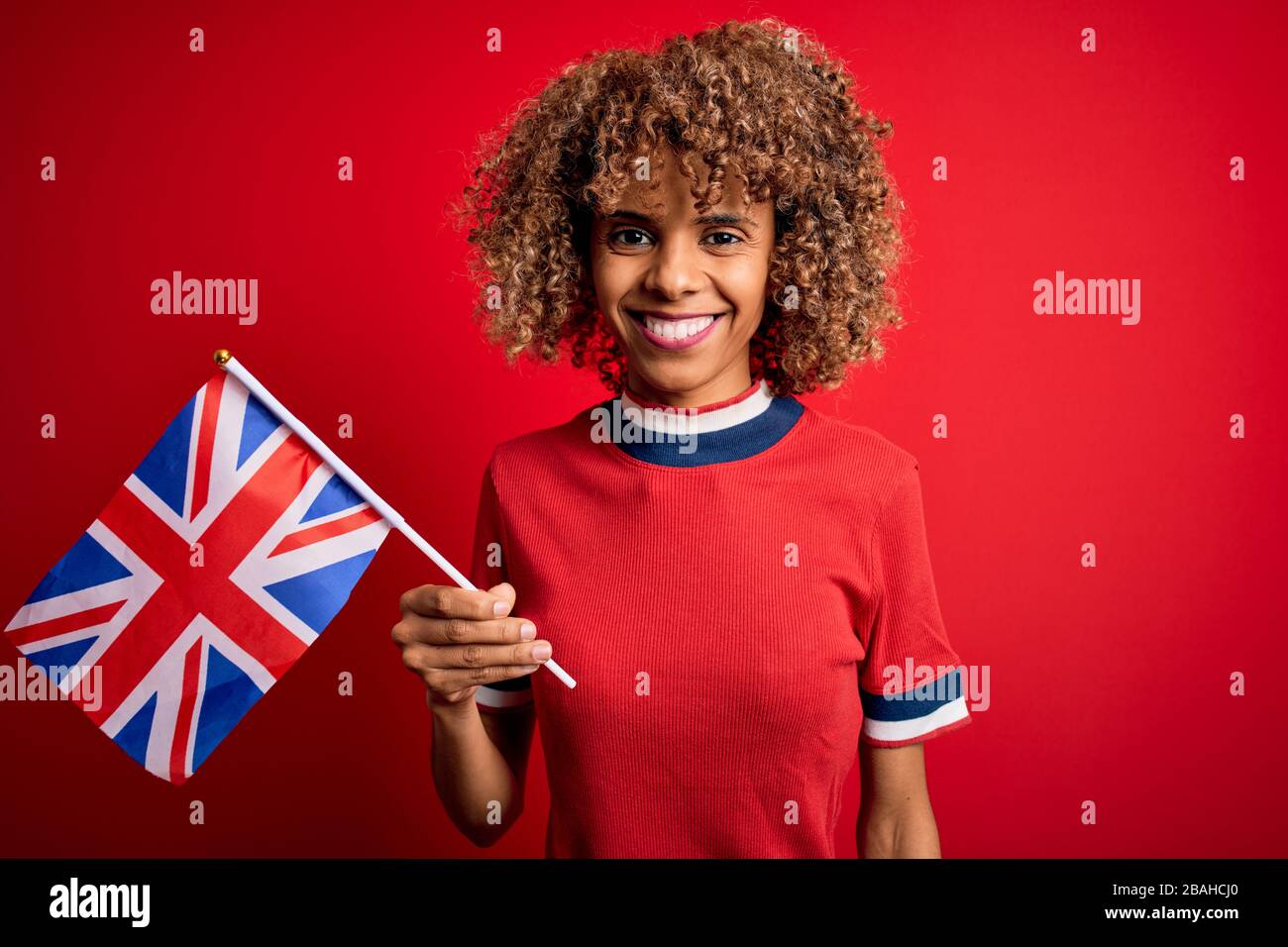 Giovane maledetta afro-americana che tiene la bandiera del regno unito per celebrare il referendum sulla brexit con un volto felice in piedi e sorridente con un sorriso fiducioso in mostra Foto Stock