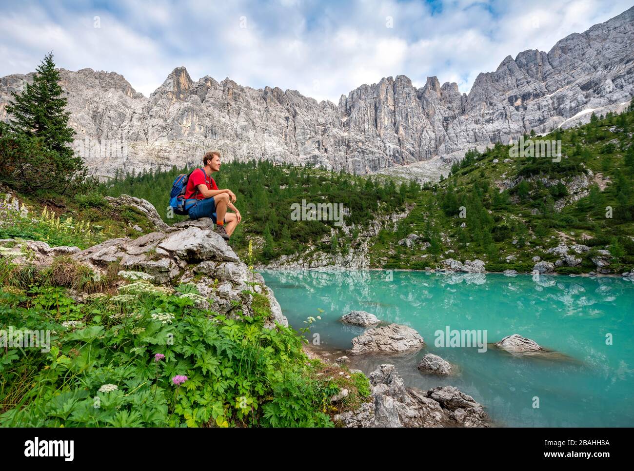 Escursionista seduto, adagiato su una roccia al lago verde turchese di Sorapis, Lago di Sorapis, Dolomiti, Belluno, Italia Foto Stock