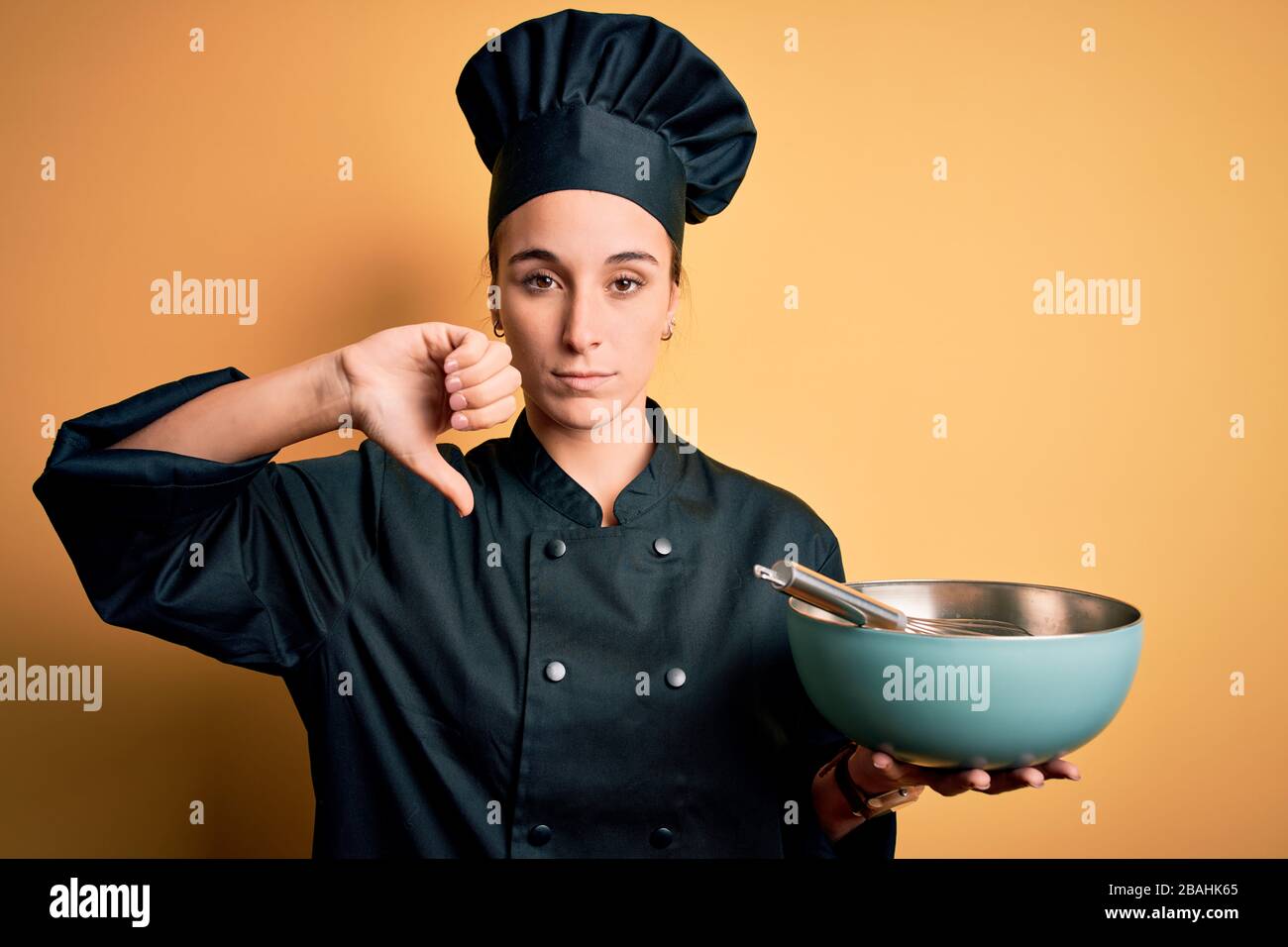 Giovane bella donna chef che indossa l'uniforme da cucina e cappello che  tiene la ciotola