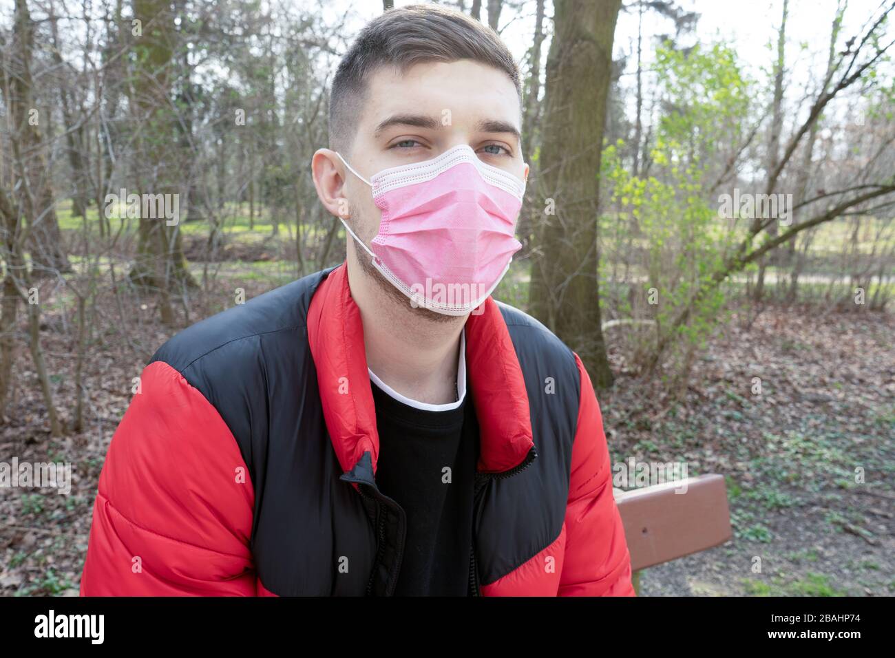 Ritratto di un uomo brunetta in un bendaggio chirurgico su uno sfondo di una foresta, coronavirus, malattia, infezione, quarantena, maschera medica Foto Stock