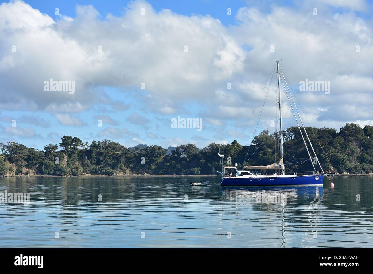 Grande yacht a vela con scafo blu e gommone a poppa ancorato in un porto calmo e pianeggiante. Foto Stock