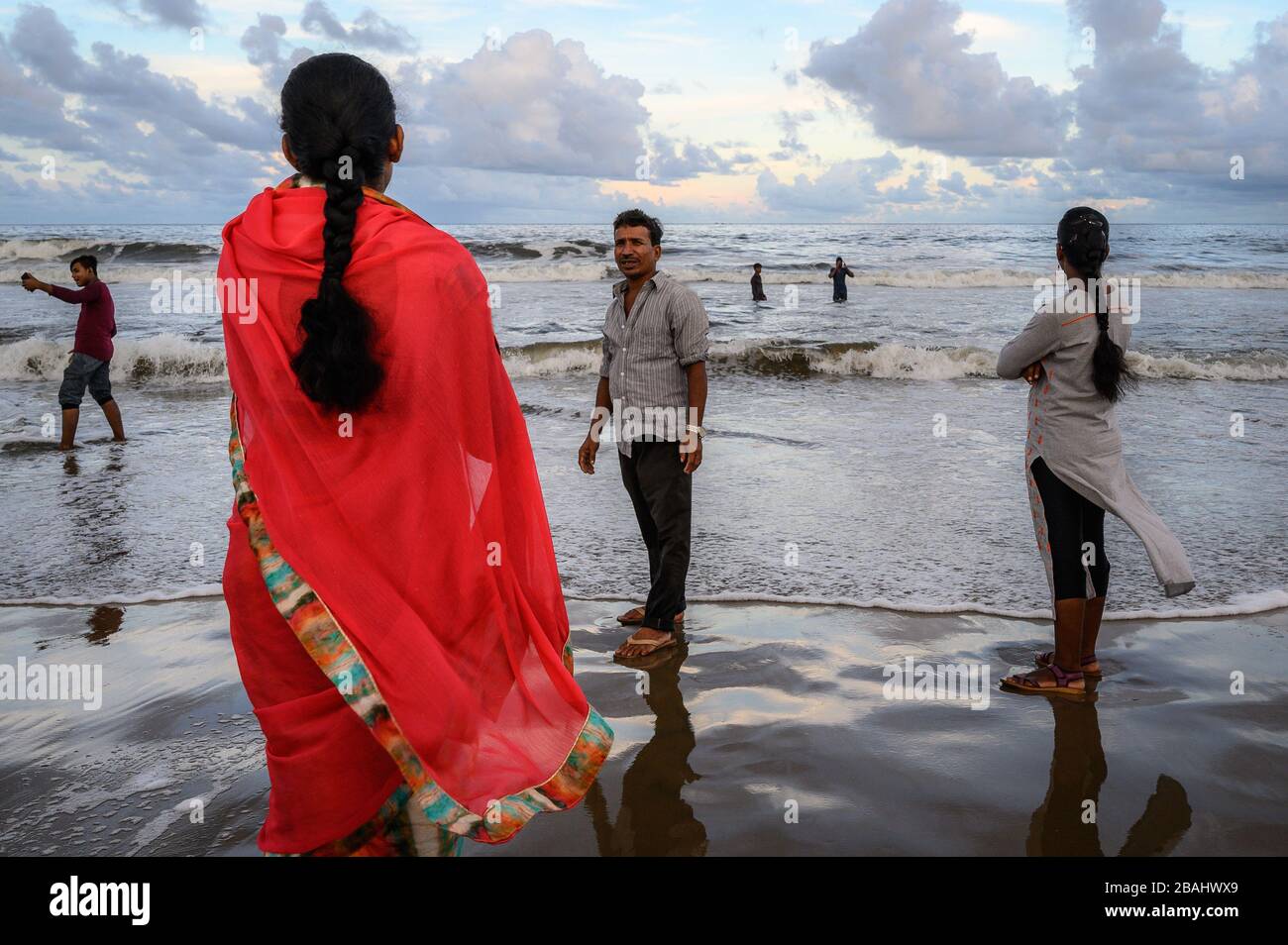Una donna in un saree rosso e altre persone sulla costa di Marina Beach, Chennai, India Foto Stock