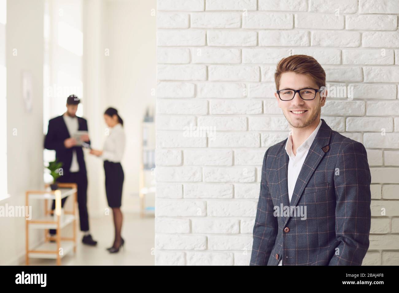 Sorridente uomo d'affari positivo in abbigliamento casual in piedi in un ufficio bianco su un muro bianco. Foto Stock
