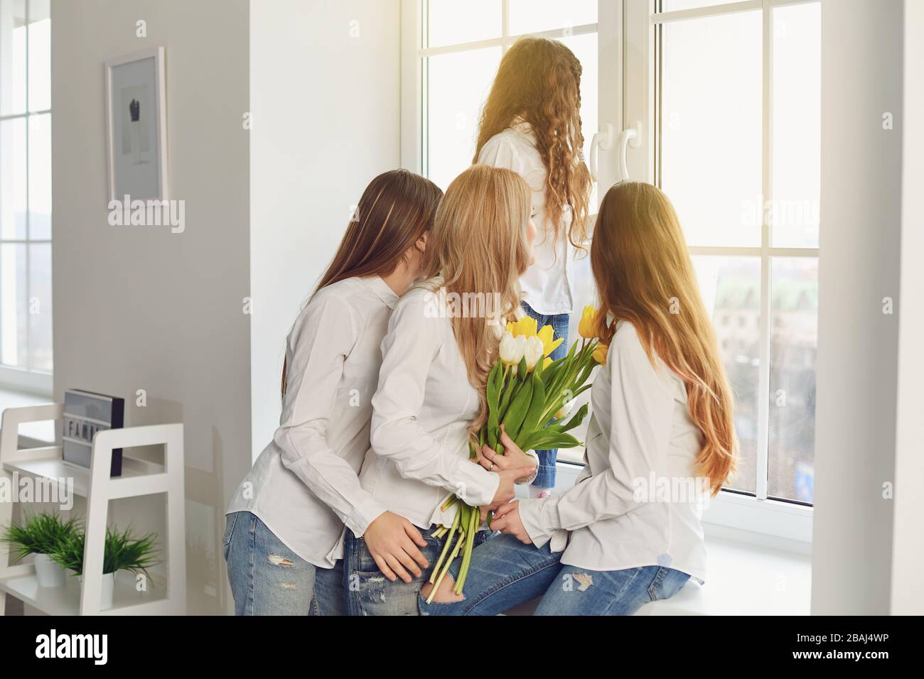 Buona festa della mamma. Una madre e tre figlie con fiori che guardano la finestra nella casa. Foto Stock