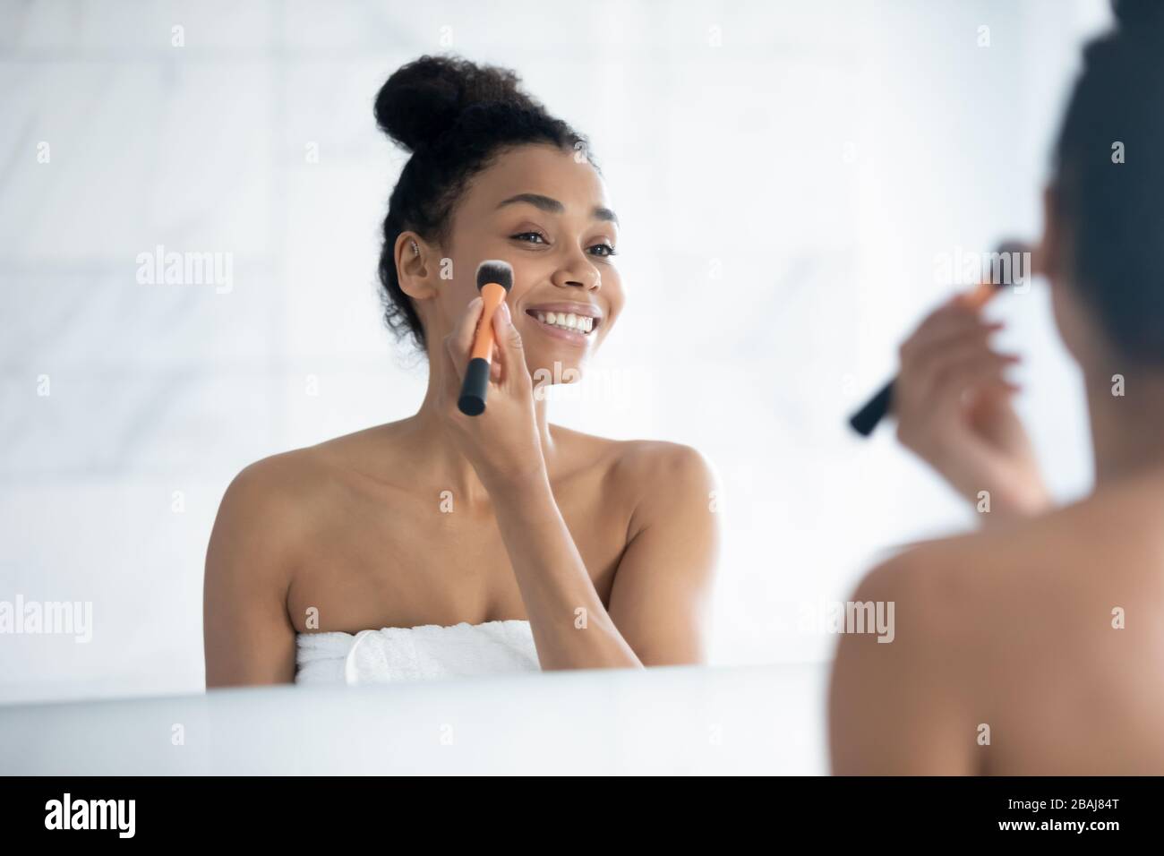 Bella donna africana tiene pennello applicare fondazione sulla faccia Foto Stock