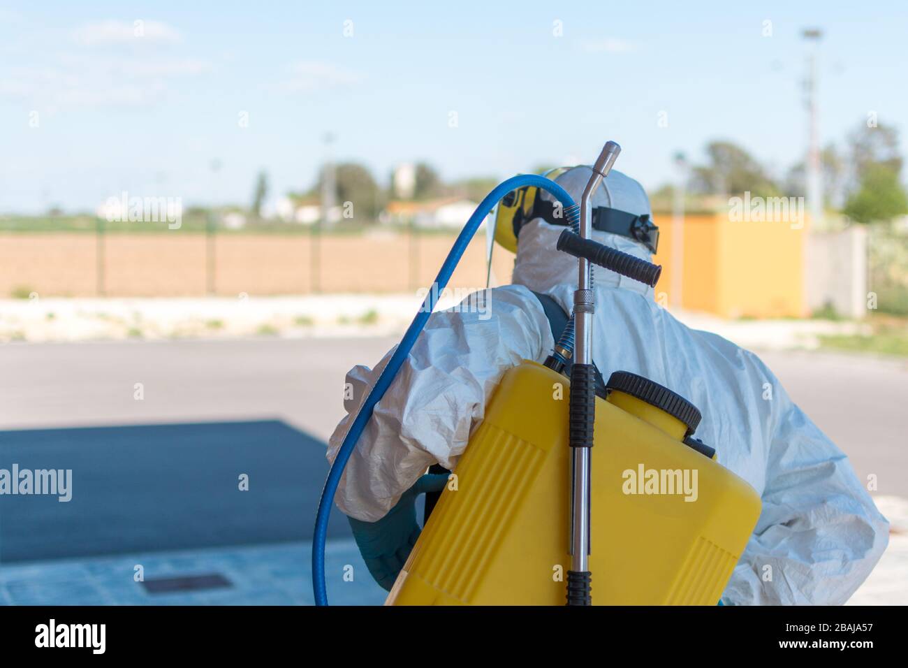 Indossando un dispositivo di protezione personale NBC, indumenti protettivi, guanti, maschera, visiera protettiva, pulire le strade con uno zaino di spray pressurizzato disinfetta Foto Stock