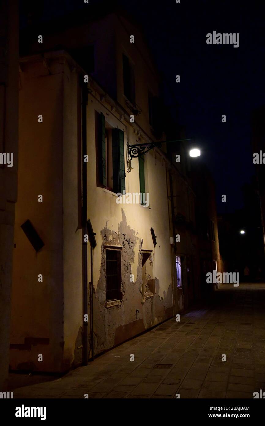 Lampada retro sulla casa veneziana che dà ampia luce in vicolo scuro sullo sfondo di una casa tradizionale fondamentalmente coperto al buio con solo luce Foto Stock