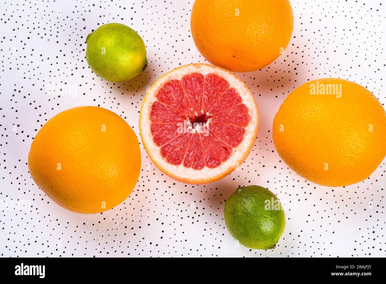tre arance intere, due limes e mezzo pompelmo sono punteggiati su una superficie bianca. fondo. succosa agrumi e vitamina alimentare Foto Stock