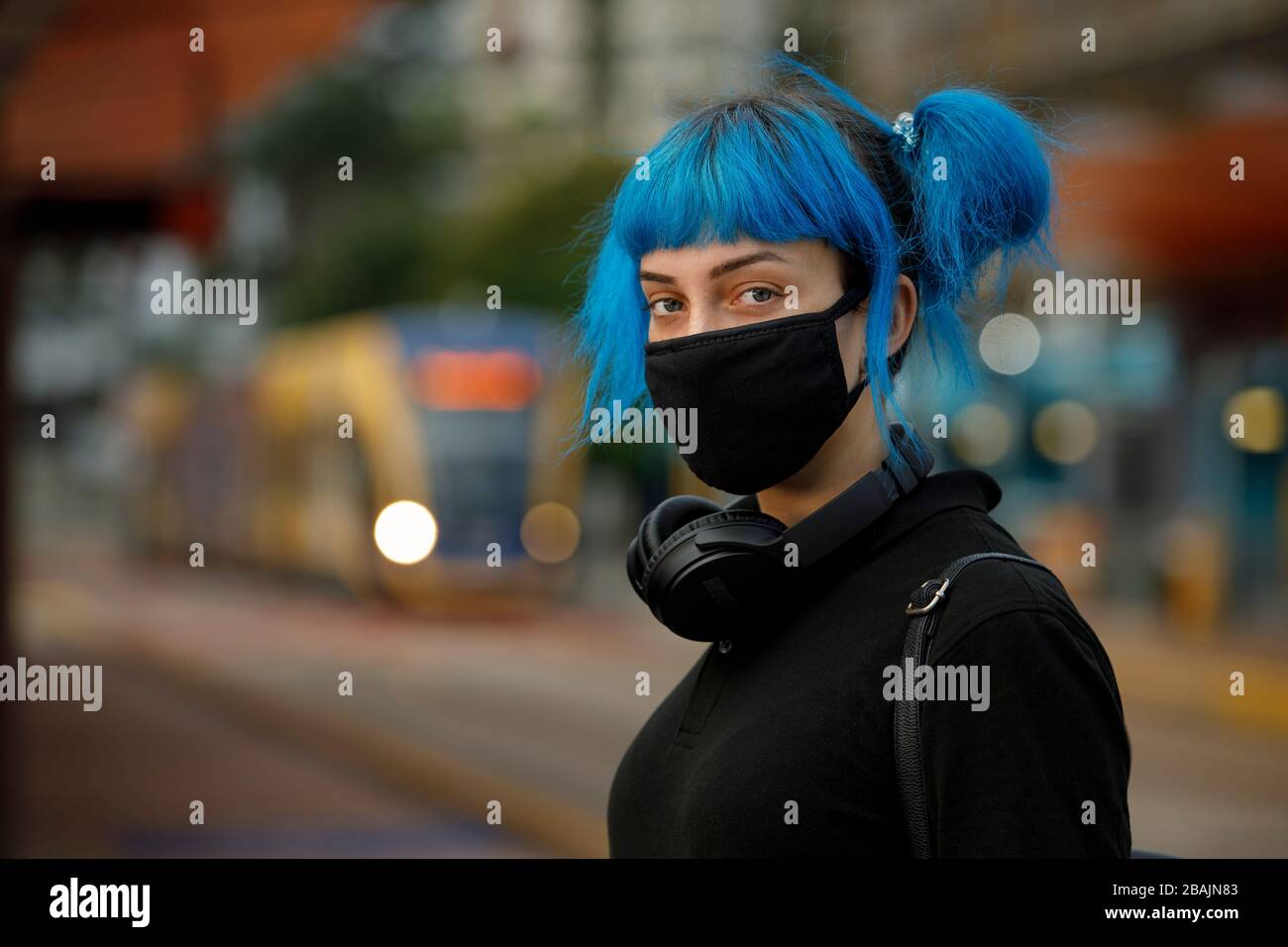 coronavirus maschera viso medico alla moda indossata da giovane studentessa con capelli blu stile anime alla fermata del tram. inquinamento dell'aria o stop covid-19 concetto Foto Stock