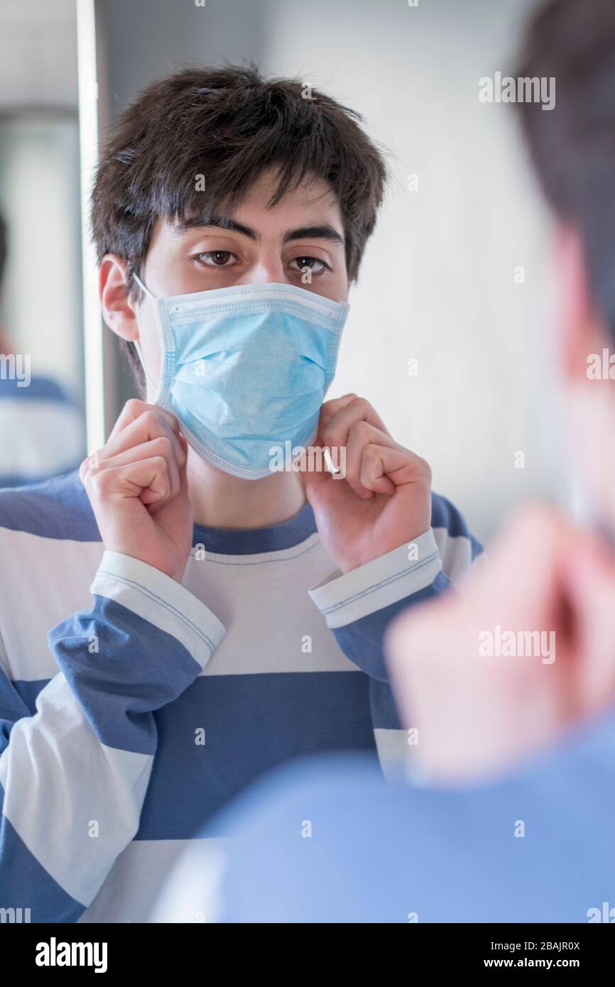 Un ragazzo adolescente che regola la sua maschera facciale nello specchio Foto Stock