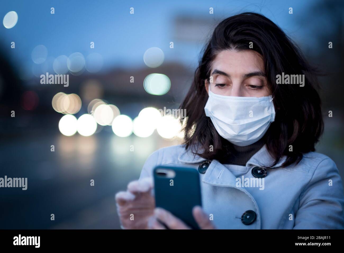 Una donna che indossa una maschera facciale e sta all'esterno durante l'epidemia di Coronavirus Foto Stock