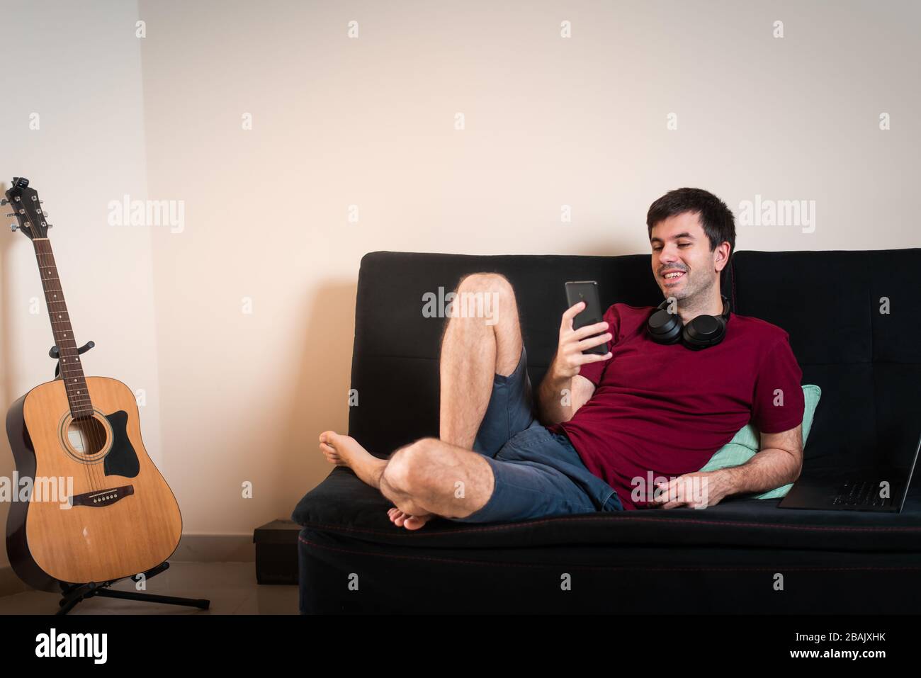 Uomo che usa il telefono mentre si siede sul divano a casa Foto Stock