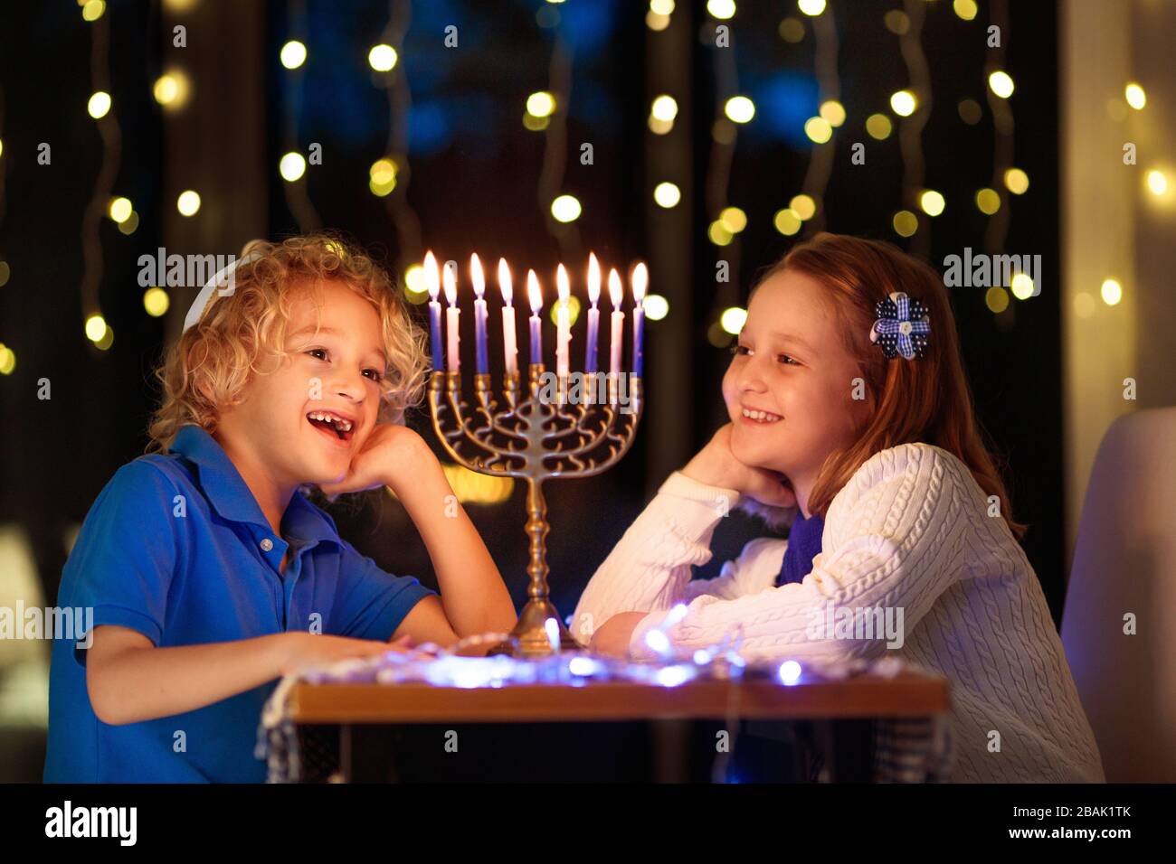 I bambini celebrano Hanukkah. Festa ebraica delle luci. Bambini che illuminano candele sulla tradizionale menorah. Ragazzo in kippah con dreidil e Sufganiyah doug Foto Stock