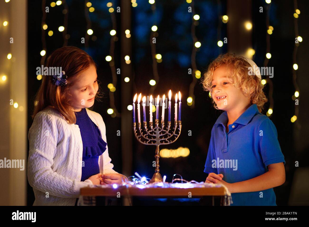 I bambini celebrano Hanukkah. Festa ebraica delle luci. Bambini che illuminano candele sulla tradizionale menorah. Ragazzo in kippah con dreidil e Sufganiyah doug Foto Stock