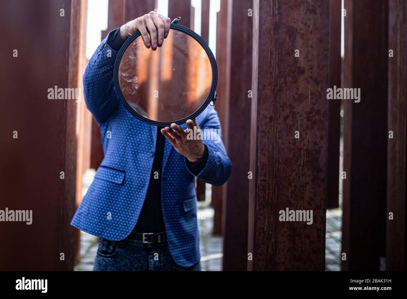 Ritratto di un giovane atleta maschile in elegante ed elegante abito tra pali in ferro grezzo e arrugginito Foto Stock