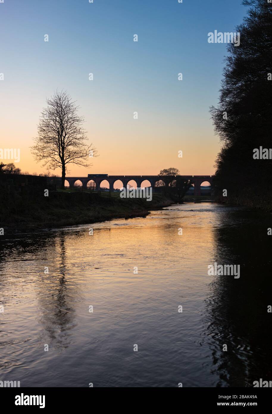 Silhouette di una ferrovia diretta servizi di classe 66 locomotiva che attraversa il viadotto di Whalley con un treno merci che trasporta materiali per la rete ferroviaria Foto Stock