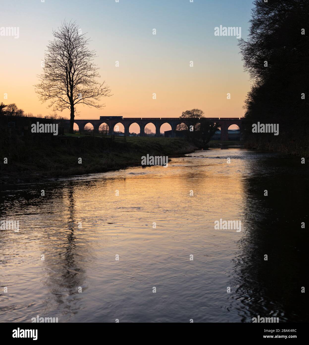 Silhouette di una ferrovia diretta servizi di classe 66 locomotiva che attraversa il viadotto di Whalley con un treno merci che trasporta materiali per la rete ferroviaria Foto Stock
