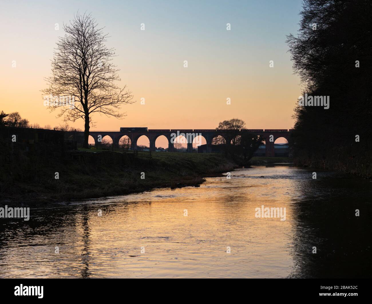 Silhouette di una ferrovia diretta servizi di classe 66 locomotiva che attraversa il viadotto di Whalley con un treno merci che trasporta materiali per la rete ferroviaria Foto Stock