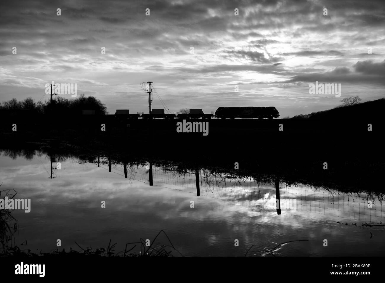 Silhouette di una locomotiva DRS classe 68 che traina fiasche nucleari al tramonto sulla linea ferroviaria della costa Cumbria al tramonto Foto Stock