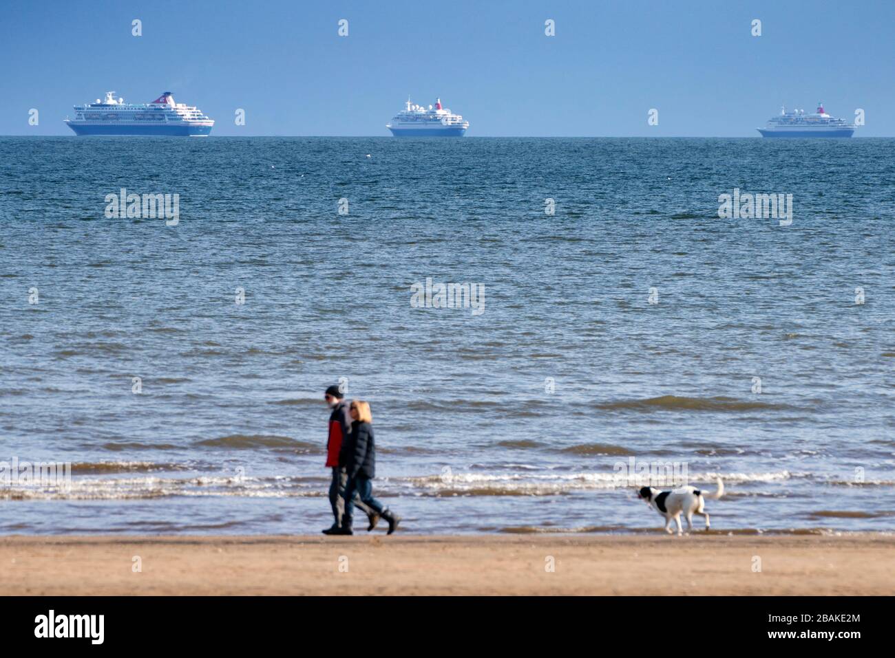 Portobello, Scozia, Regno Unito. 28 marzo 2020. Il primo fine settimana del coronavirus lockdown il pubblico erano all'aperto esercizio e mantenere distancing sociale lungo il lungomare di Portobello. Foto persone che camminano cane sulla spiaggia con tre navi da crociera fuori servizio da Fred Olsen all'ancora in distanza. Iain Masterton/Alamy Live News Foto Stock