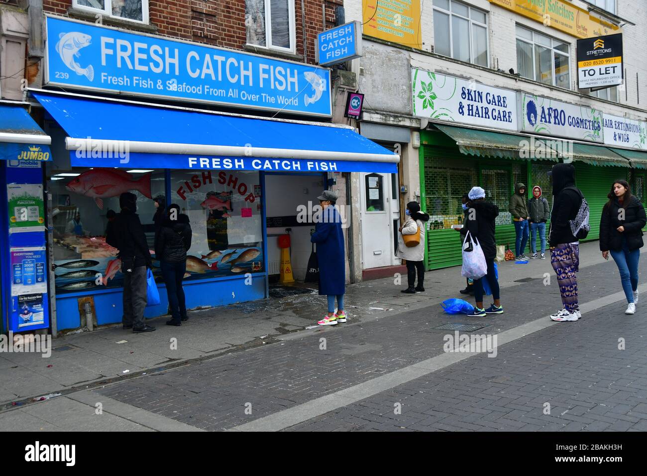 Londra, Regno Unito. 28 marzo 2020. Un uomo di sicurezza durante il coronavirus nel Regno Unito ha bloccato la gente fuori la coda di shopping alla parte anteriore di un negozio di pesce, il 28 marzo 2020, al mercato di Walthamstow, Londra. Credito: Picture Capital/Alamy Live News Foto Stock