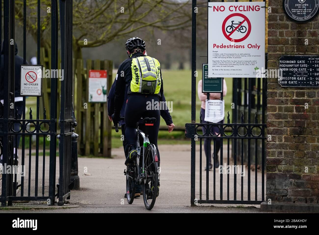 Un ciclista passa davanti a un cartello che dice che i ciclisti sono vietati dal Richmond Park a causa dell'elevato volume di distanziamenti sociali che compromettono. Mentre il Regno Unito continua a bloccarsi per contribuire a frenare la diffusione del coronavirus. Foto Stock
