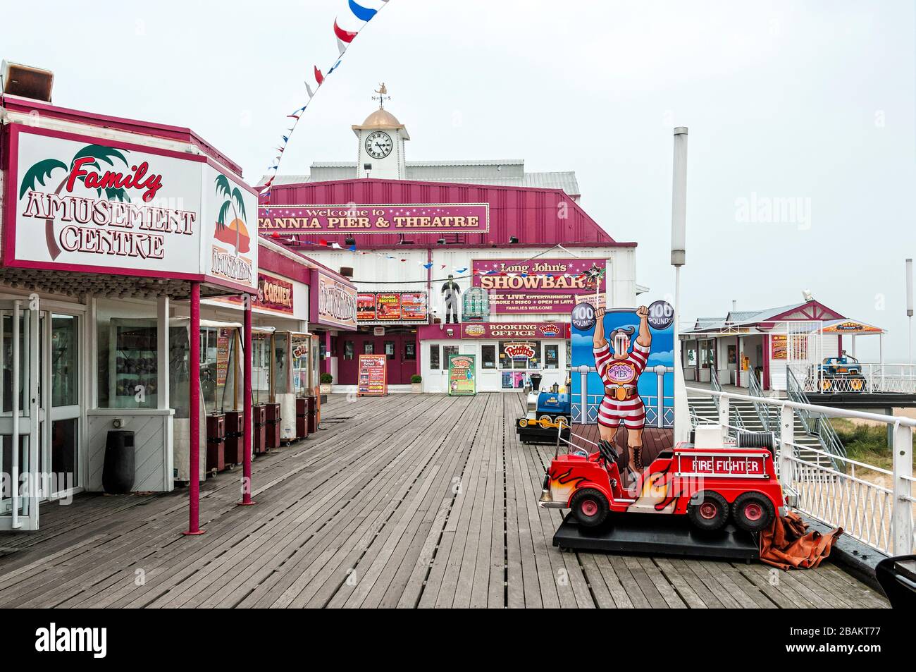 Un grande teatro si trova in fondo a una fila di portici di divertimento con colorati poster che pubblicizzano futuri spettacoli accanto alle scale per una spiaggia di sabbia Foto Stock