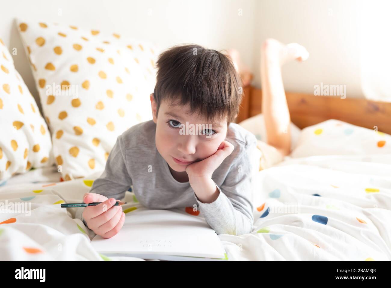 Ragazzo della scuola a letto e fare i compiti della scuola a casa, scrivendo in quaderno. Formazione online a distanza. Quarantena Foto Stock